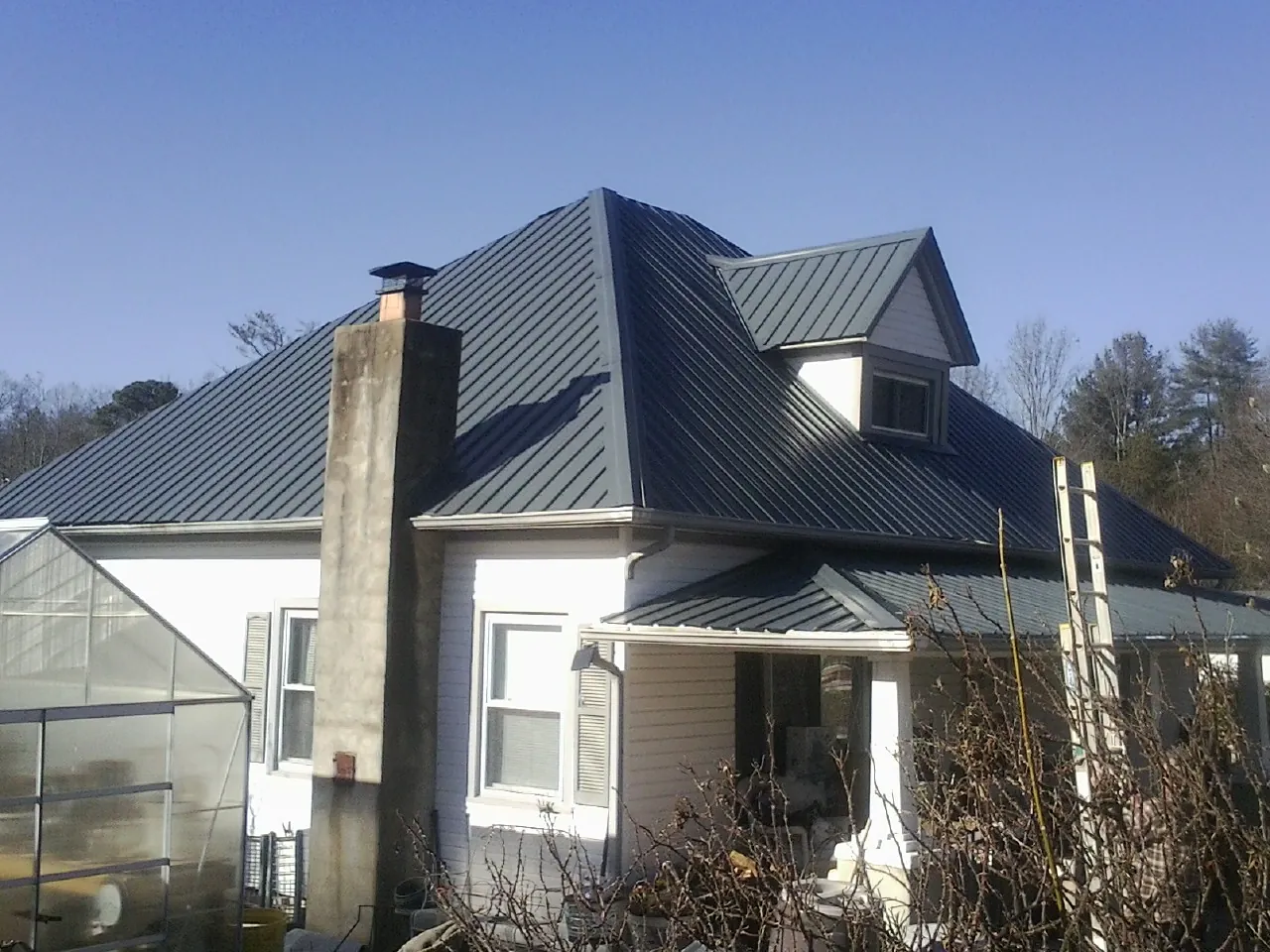 Dark blue standing seam metal roof on a white farmhouse with dormer — Slate & Tile Roof Repair by Roofing Brothers in Galesburg