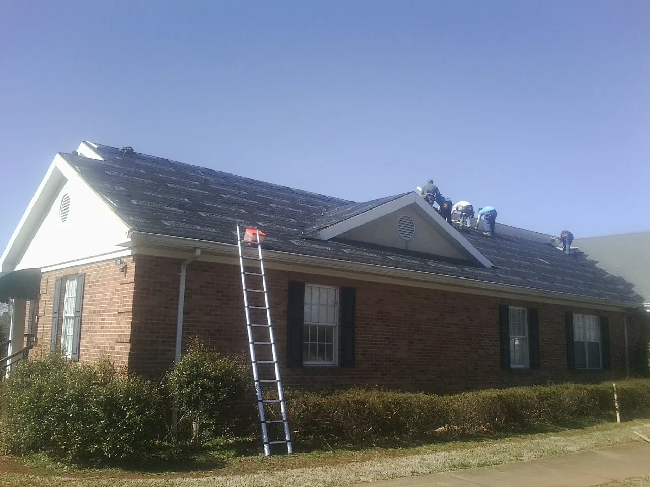 Crew tearing shingles off a brick ranch roof with a ladder set — Emergency Roof Repair work by our crew in Galesburg