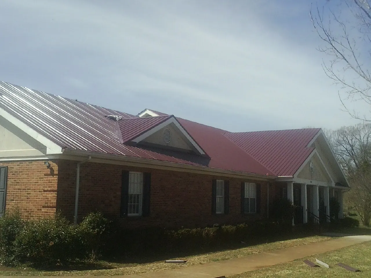 Red metal roof with gabled entries on a long brick building, from a Hail Damage Roof Repair job in Galesburg