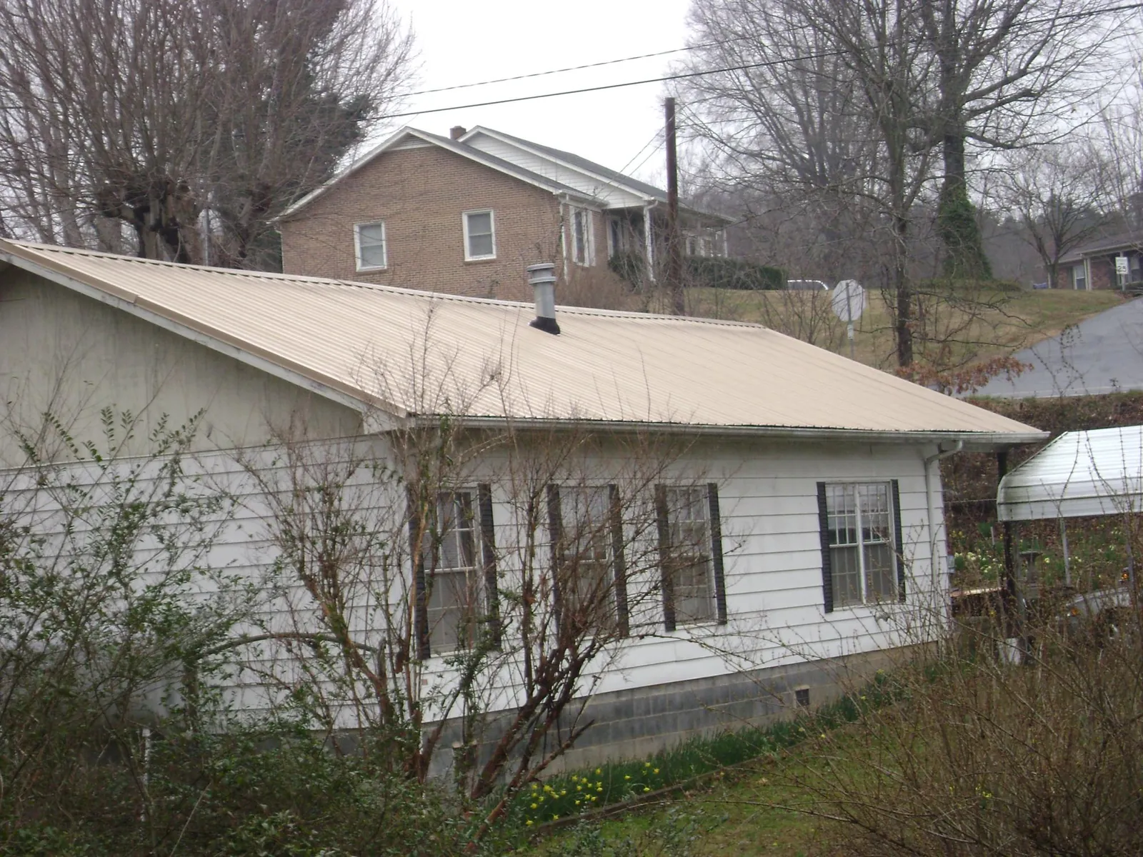 Tan metal roof on a white sided house set into a hillside — Commercial Roofing by Roofing Brothers in Galesburg