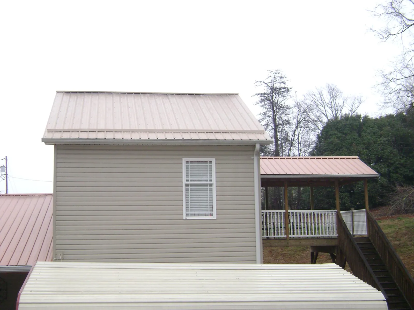 Tan metal roofs on a two story addition and attached porch, from a Roof Replacement job in Galesburg